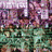 Pixelated image with teal text on black background, showing blurred floral and greenery elements in the top-left corner.