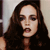 Pixelated close-up of a person with long dark hair, light skin, and dark eye makeup, mouth slightly open, wearing a dark top against a light background.