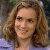 A pixelated close-up of a person with light brown curly hair wearing a light blue top against a blurred background.