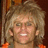 Static pixelated image of a person with light brown curly hair, visible ear, and orange clothing against dark background.