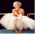 Pixelated image of a person in a white tutu-like dress with arms crossed, standing against dark background.