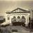 Pixelated grayscale image of a classical building facade with columns and a triangular pediment, set against a gradient background.