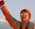 A 4-frame animated contact sheet showing a person in an orange hooded jacket holding red objects against a mountainous sky background with varying facial expressions and mouth positions across frames.
