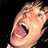 Pixelated close-up of a person's face with mouth open in a shout or yell, dark background, visible teeth and tongue.