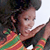 A pixelated close-up of a person with dark curly hair wearing a colorful striped shirt, holding a dark object near their face.