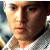 Pixelated close-up of a person's face with light skin tone, brown eyes, and dark hair, wearing a white collared shirt against a blurred background.