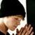 Pixelated static image of a person in profile wearing a black beanie and white shirt with brown accents, cropped to show upper body against dark background.