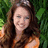 Pixelated image of a person with long brown hair wearing an orange top against green foliage, with blue background text and symbols.