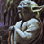 Pixelated static image of a character with green skin, large ears, and a light-colored headpiece holding a white object against a dark background.