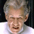 Static pixelated image of a person with light brown hair, wearing a white collared shirt against a dark background.