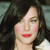 Pixelated close-up of a person with dark hair, light skin, and red lips, wearing a light-colored top against a muted background.