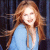 A pixelated static image shows a person with long light brown hair wearing a light blue top against a dark background.