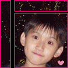 A person with short dark hair and light skin appears in a static image with a pink heart symbol at the bottom right corner against a dark background with scattered light specks.