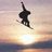 Pixelated silhouette of a figure in mid-air against a sunset sky with gradient hues from orange to purple.