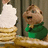 Animated pixelated character in green shirt with brown hair, standing behind stack of coins and white object against wooden background.