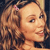 A static pixelated image of a person with light brown curly hair, a small pink bow on the left side, and a neutral expression against a dark background.