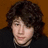 Pixelated image of a person with curly brown hair and dark clothing against an orange background, next to cyan text on black.