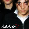 Two people in close-up; one wears a black zip-up jacket with white text and red dots, the other has a white collar visible.