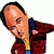 Pixelated static image of a bald man in a red jacket with blue collar and yellow shirt, leaning forward with one arm extended.