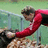 A pixelated figure in a red long-sleeve top and dark pants leans forward with arms extended toward a brown textured surface, set against a greenish background.