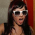 A pixelated image of a person with long dark hair wearing white-framed sunglasses and a black sleeveless top against a red and gray background.