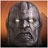 Pixelated close-up of a humanoid face with metallic gray skin, glowing white eyes, and an open mouth showing teeth against an orange gradient background.