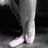 Pixelated grayscale image of a person's lower legs and feet wearing light-colored pants and white shoes against dark background.