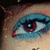 A close-up of a stylized eye with blue eyeshadow, red eyeliner, and brown iris, set against light skin.