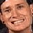 A pixelated image of a person with short hair and a dark cap, smiling widely against a black background with white text blocks.