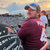 Pixelated static image shows two figures near water at dusk; one figure in maroon shirt and dark cap faces left, another in light shirt faces right, both partially obscured by pixelation.