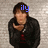 A person in a black jacket with red accents stands against a light brick wall, blue text above their head changes from 'ily' to '<3'.