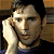 Pixelated close-up of a person with dark hair resting their right hand against their cheek, wearing a light-colored shirt under a darker outer layer.