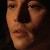 A pixelated close-up of a person's face with warm skin tones, dark hair, and a neutral expression against a dark background.
