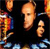 Pixelated image of a person with light skin tone wearing dark clothing, standing against a dark background with colorful abstract shapes on the left and right edges.