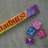 A static image shows a colorful candy bar and four small square candies on a gray surface, with purple pixelated text surrounding the image.