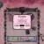 Pixelated static image of a light gray rectangular device with dark borders, displaying a pink screen showing faint text and a small green element.