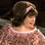 A pixelated image of a person with brown hair wearing a light pink off-shoulder top against a dark background.