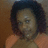 Pixelated image of a person with dark curly hair wearing an orange sleeveless top against a brown background.