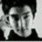 Black-and-white image of a person with dark hair wearing a dark top, hand near face in three showing slight head movement
