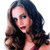 Pixelated image of a person with long dark brown hair, wearing a dark top, and a light-colored garment with a pinkish hue, set against a plain white background.