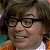 Pixelated close-up of a person with dark hair and glasses, wearing an orange garment against a blurred background.