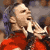 Pixelated static image of a person in red clothing holding an object near their mouth against a blurred background.