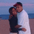 Two people embrace on a beach at dusk, one wearing white and red cap, the other in dark clothing.