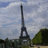 Pixelated static image of a tall iron lattice tower against a cloudy sky with greenery below.