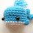 Blue crocheted whale with black eyes and white teeth, positioned on a light background.