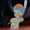 A cartoon character with orange hair and blue headband stands with arms crossed, holding a drumstick, wearing a light shirt with a flower and pink pants.