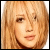 A pixelated close-up of a person with light brown hair and fair skin, showing two states: one without a heart symbol in the top-left corner and another with a small black-and-white heart icon.