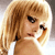 Pixelated image of a person with light brown hair styled in a side ponytail, holding a phone to their ear with a neutral expression.