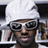 Pixelated image of a person wearing white headwrap and sunglasses with text elements on black background.