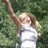Pixelated image of a person with light brown hair wearing a white sleeveless top, arm raised, against a green foliage background.